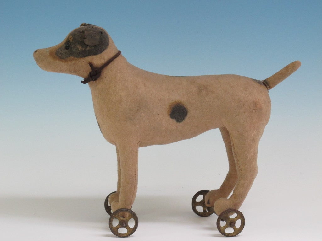 An early pull toy dog with a pair of cast iron wheels.  The body appears to be a felt cloth with stuffing and black glass eyes.  Good condition with minor wear.