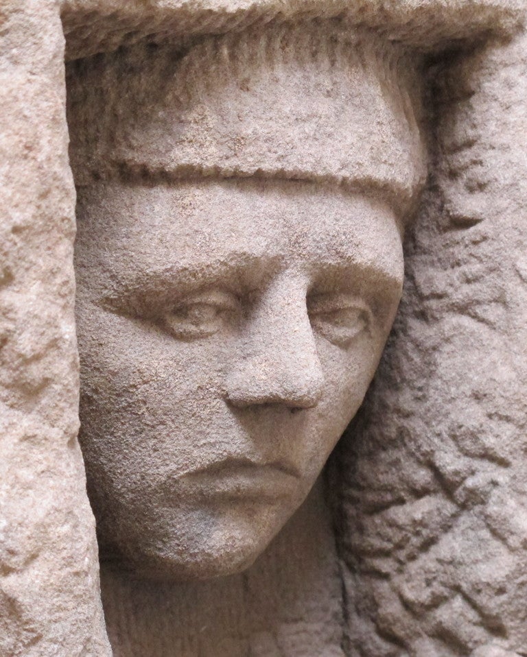 This head is carved in a block of sandstone that was probably part of a building gazing down.. The head is expressively carved with finely modeled features  contrasted to the textured recess. Mounted floating above a metal base.  Height on base 14
