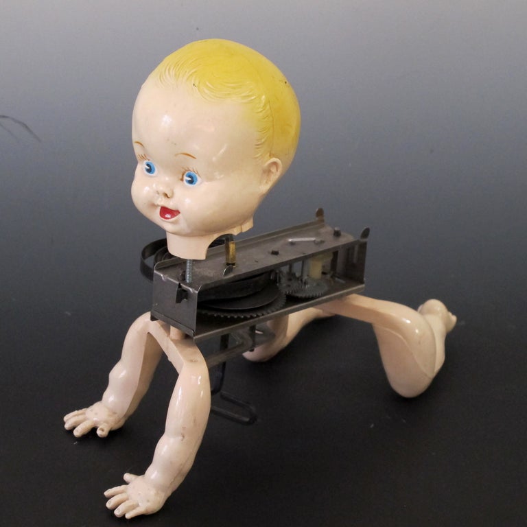 Key wind metal mechanism attached to the joined pair of plastic arms and legs with painted baby head on top.  I have collected robotics and have searched for a mechanical doll from the 1950s for some time.  A tin cover went over the motor and is