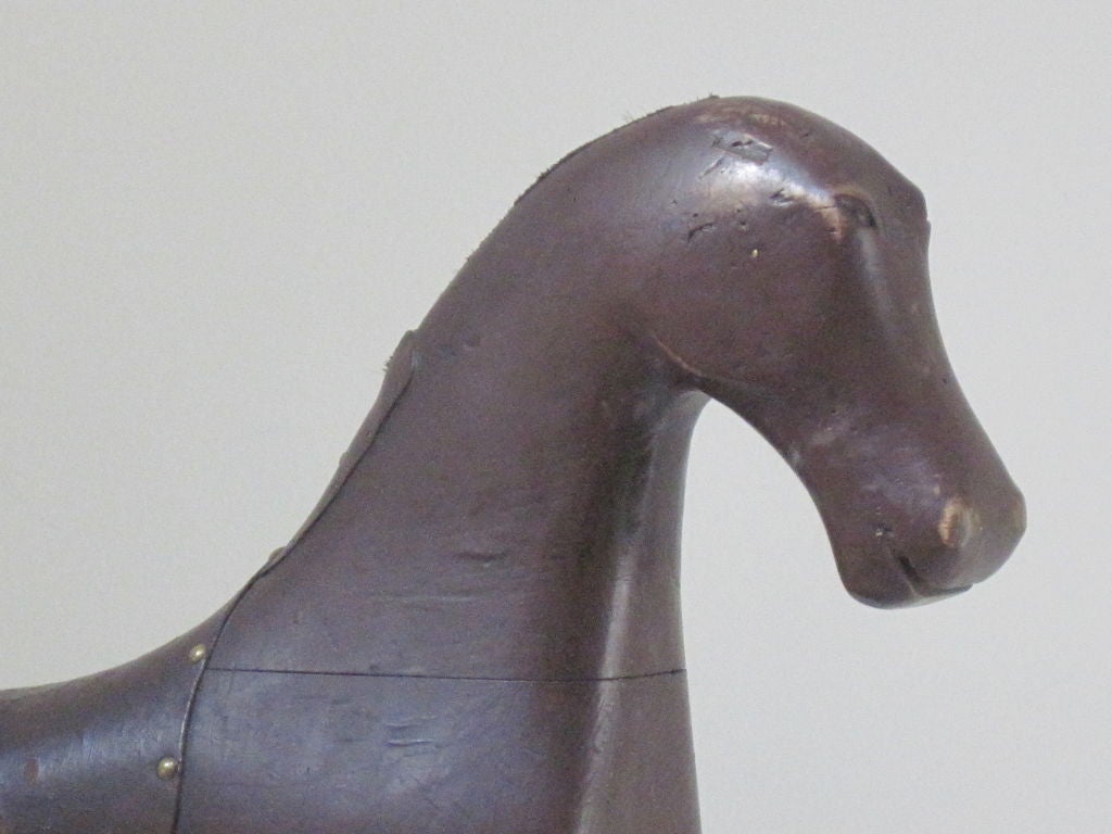 Carved and painted wood horse with leather saddle applied with brass tacks. This horse was probably made for a fortunate child and attached to a platform with wheels to be pulled or rode.It has the naive proportions of a horse with shortened legs