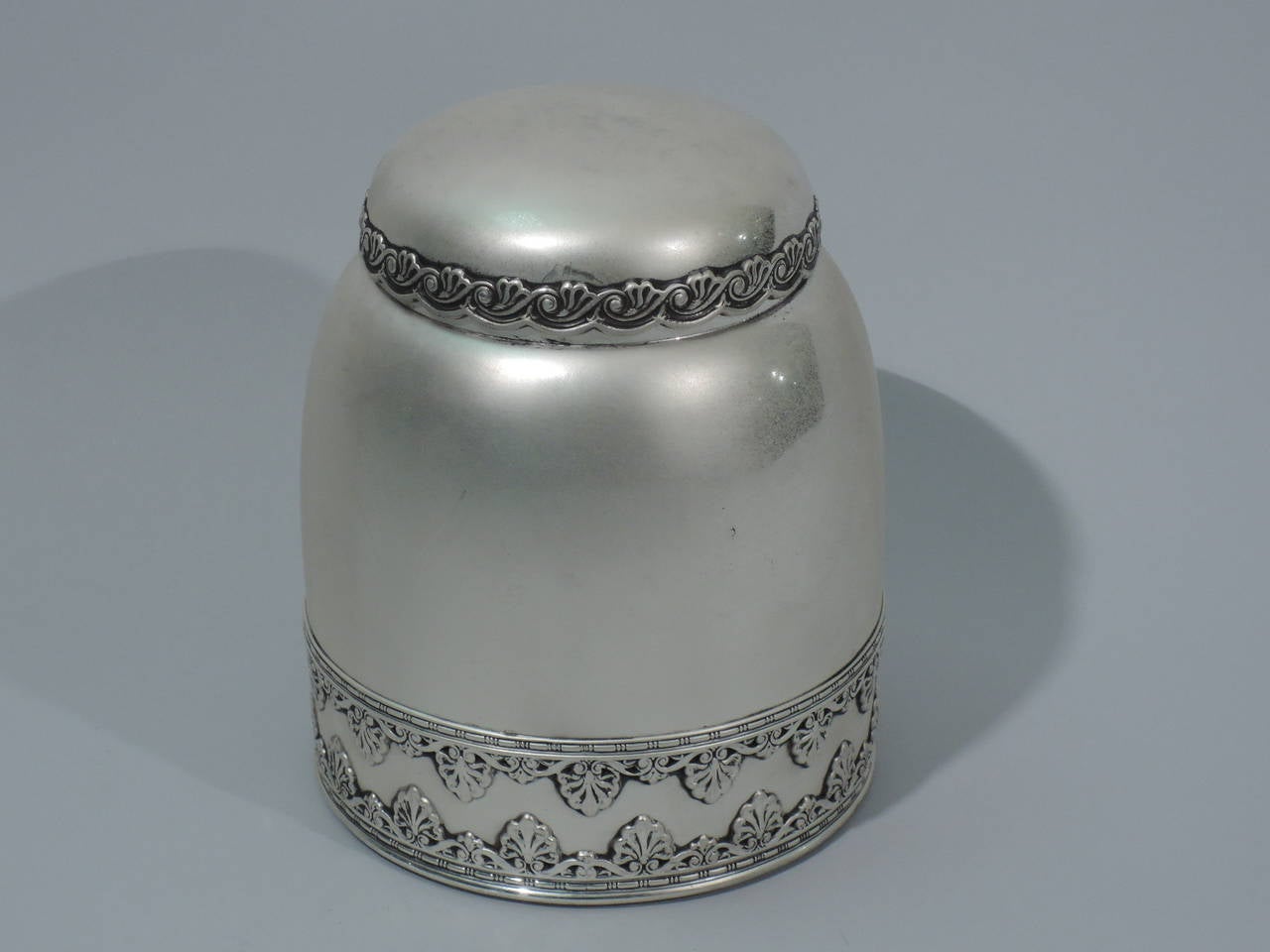 Sterling silver tobacco jar with classical ornament. Made by Whiting in New York, ca. 1890. Upward tapering sides, curved shoulder and hinged and round cover. At bottom are applied bands of palmette and bead and reel ornament. Cover rim is scalloped