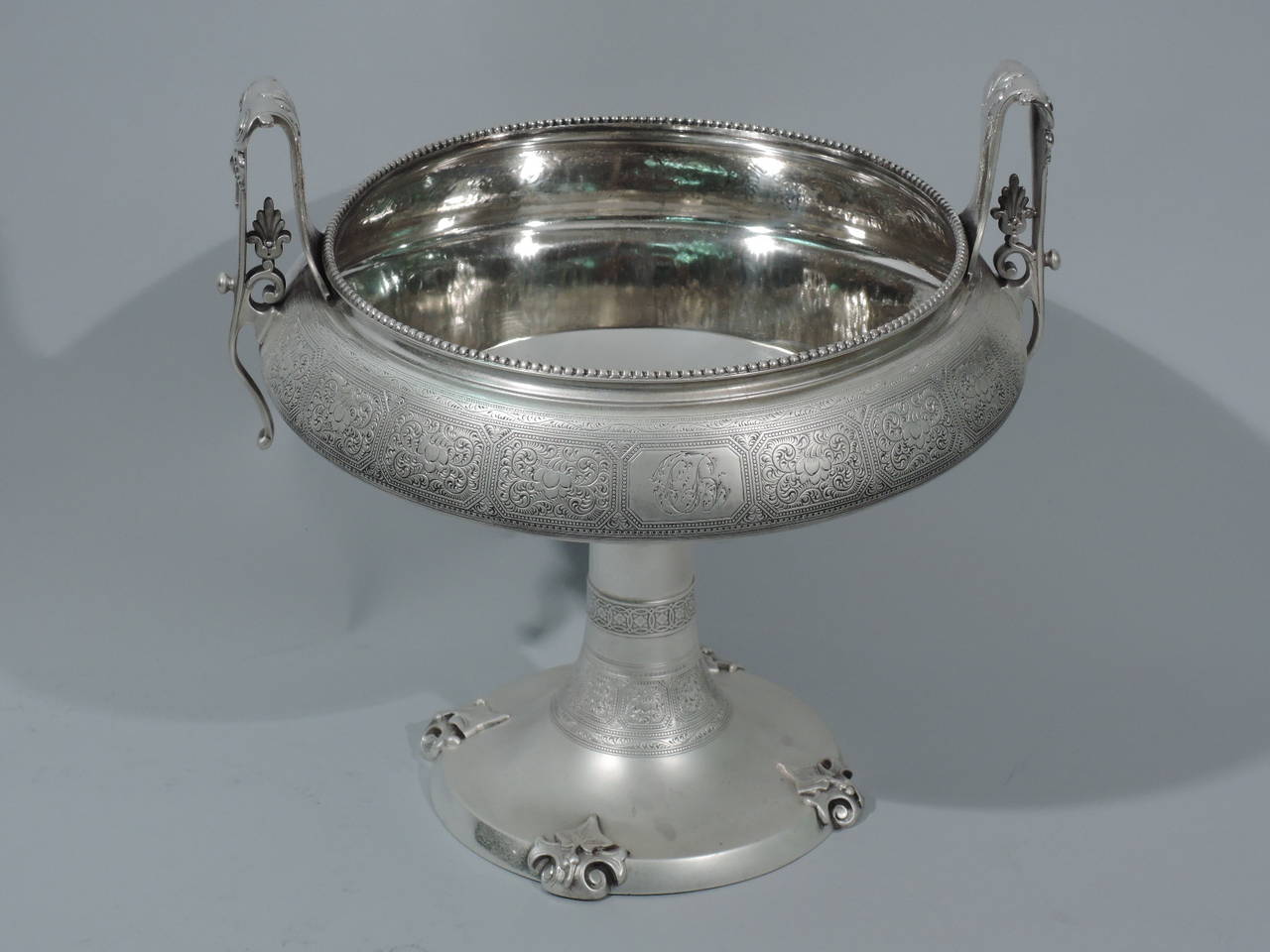 Greek Revival sterling silver bowl. Made by Tiffany & Co. in New York, circa 1870. 

Inspired by Greek kylix, the bowl is wide and shallow, and rests on conical support. Side bracket handles with volute scrolls and foliage. Dentil rim. Rectangular
