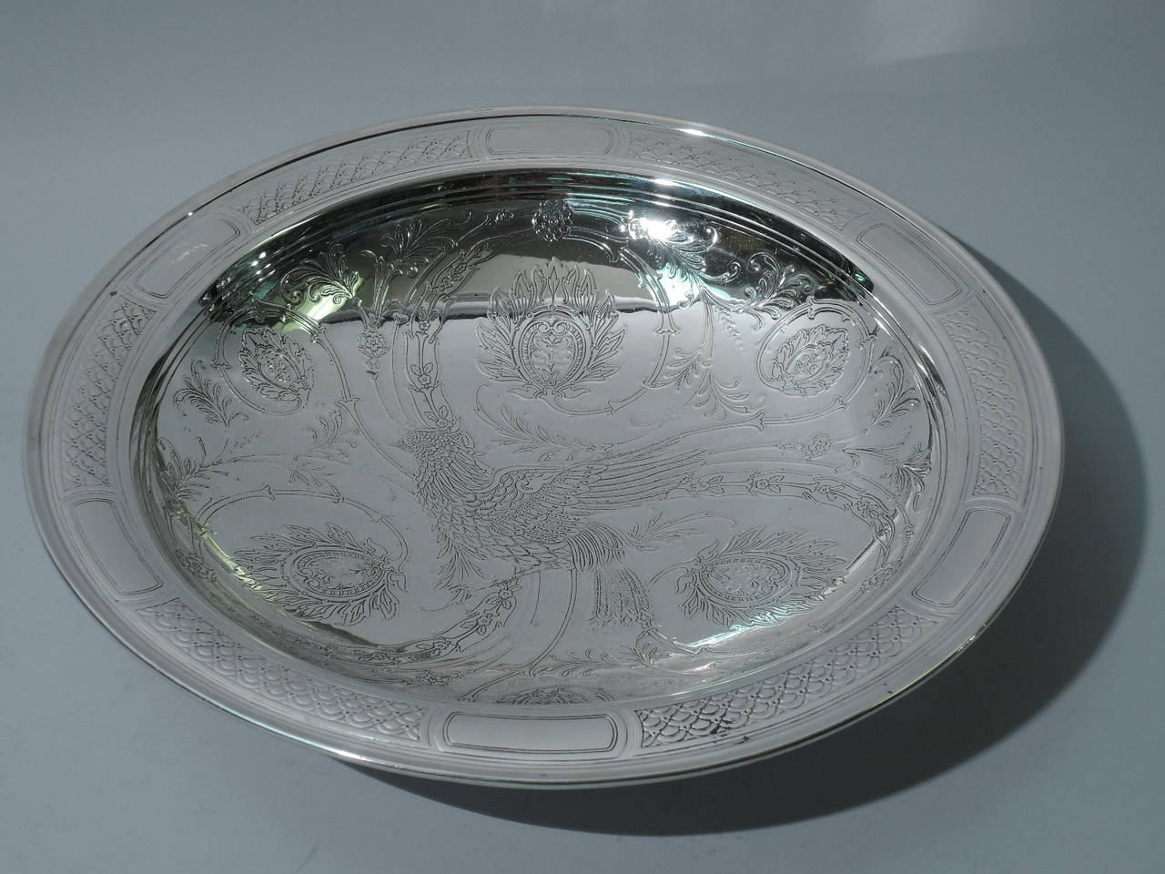 Large and shallow sterling silver bowl with bird. Made by Tiffany & Co. in New York, circa 1914. Curved sides and flat and molded rim. Rests on foot ring. Interior is acid-etched: a bird on ground with scrolls, foliage, and flowers. Rim has tubular