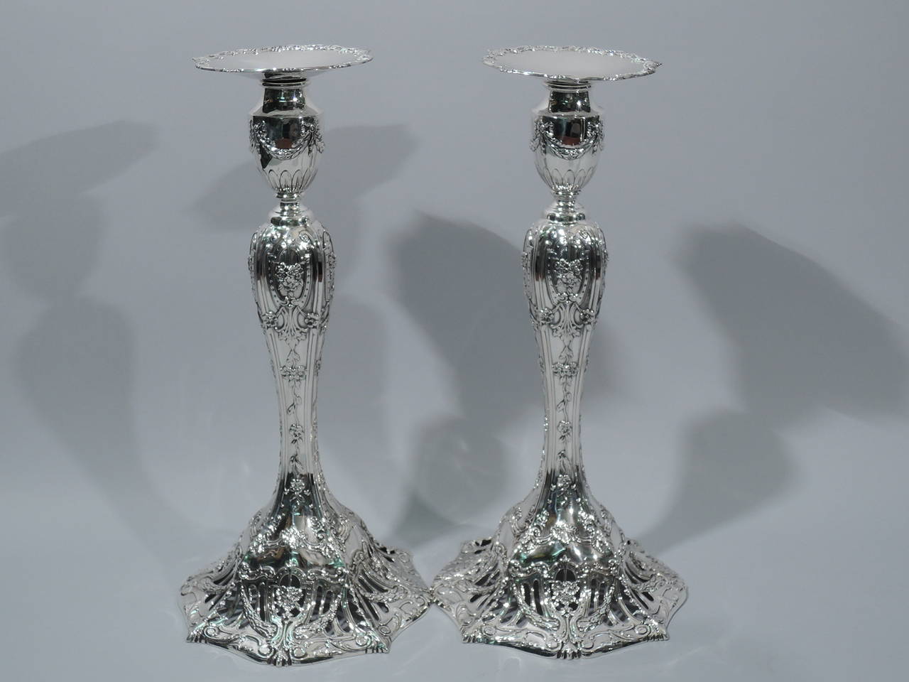 Pair of tall and fancy sterling silver candlesticks. Made for JE Caldwell in Philadelphia, ca. 1909. Each: baluster shaft, faceted dome foot, urn socket, and detachable bobeche. Raised ornament includes strapwork frames inset with bouquets, scrolls,