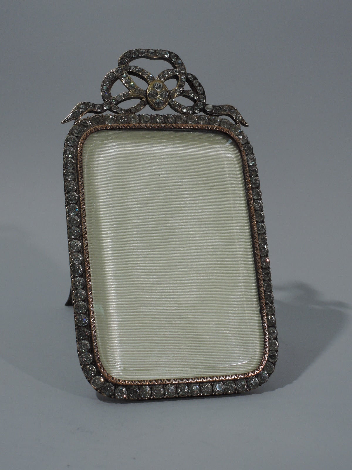 Fancy and flamboyant picture frame, ca. 1920. Rectangular with curved corners. Raised triangles and inset rhinestones. More rhinestones set in elaborate bow crown. A real show stopper. For vertical display. With beveled glass, silk lining, and
