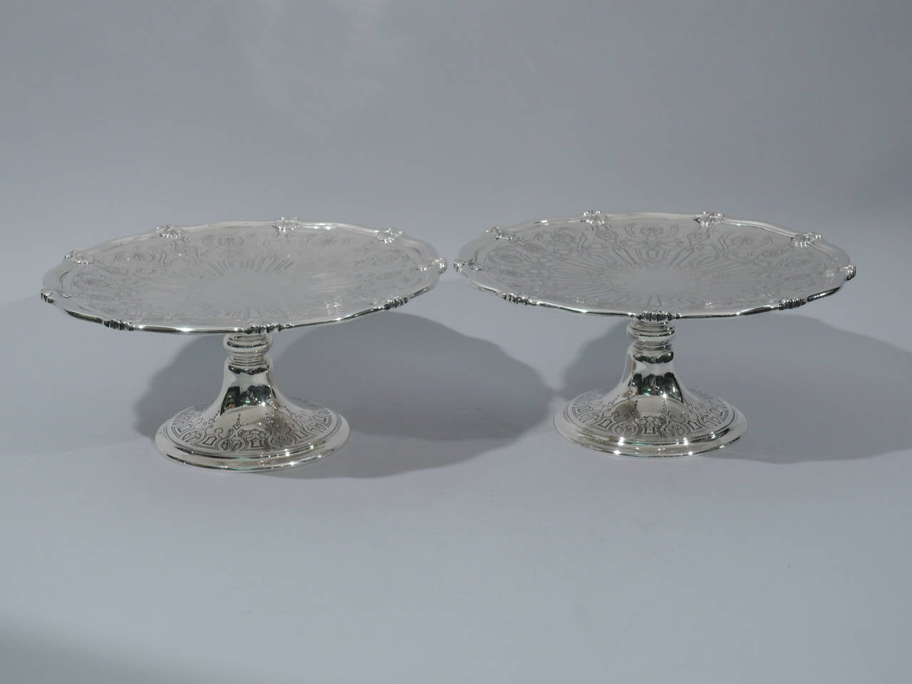 Pair of sterling silver compotes. Made by Tiffany & Co. in New York, circa 1915. Each: shallow bowl with plain centre (vacant) radiating acid-etched curvilinear ornament. Rim is scrolled with chased scallop shells. Raised and knopped support with