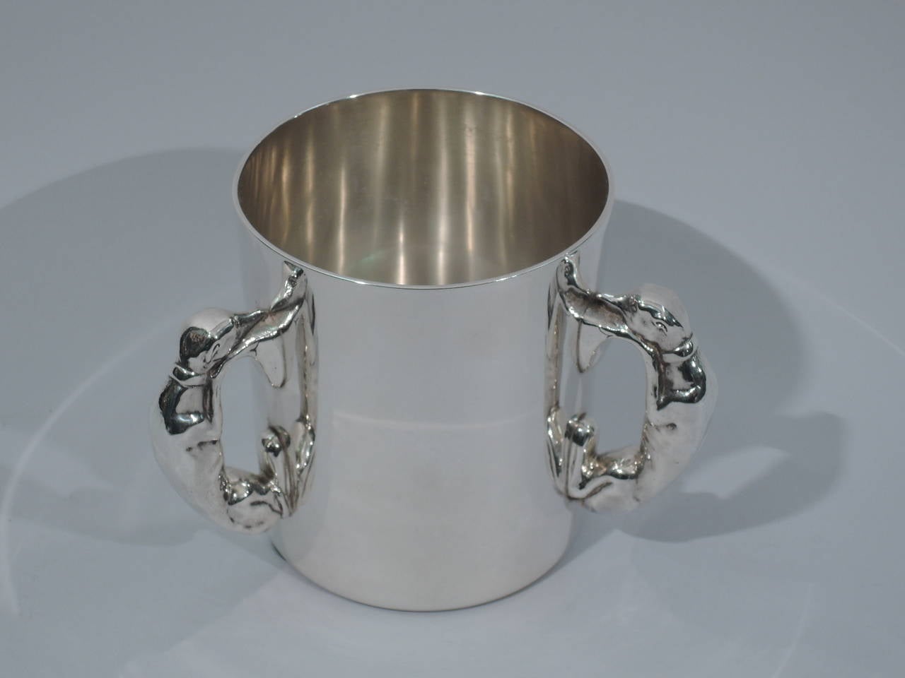 Sterling silver trophy cup with three figural dog handles. Made by Gorham in Providence, circa 1920, for Black, Starr & Frost in New York. 

Cylindrical body with C-scroll handles in form of a dog (probably whippet). Dog’s head rests on front