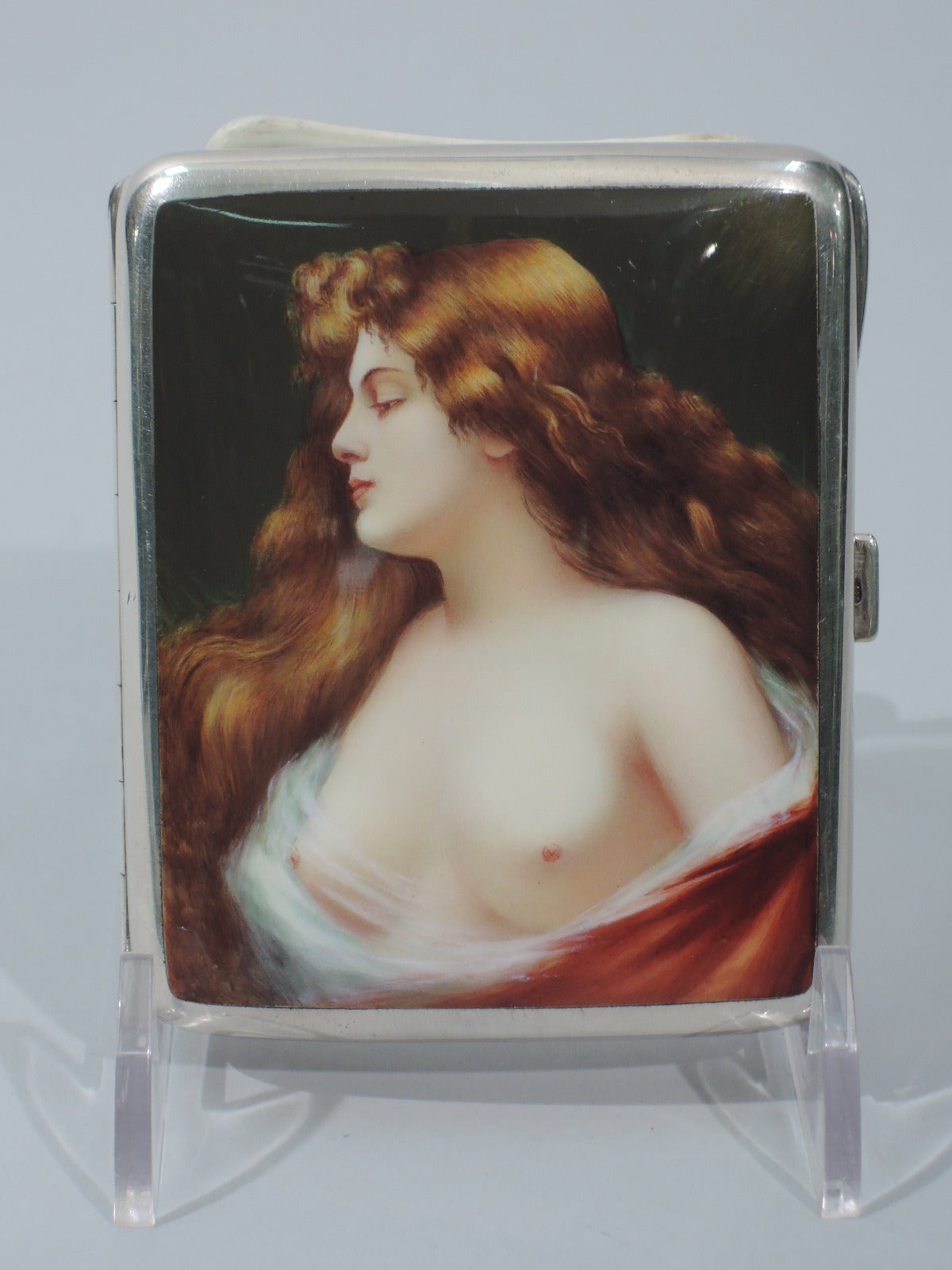 European sterling silver and enamel cigarette case. Imported to Birmingham in 1905 by Steinhart & Co. Rectangular and hinged. On cover is bust of long-tressed temptress with rose-tinted flesh swathed in red robe. Full frontal. For PG-13 version, see