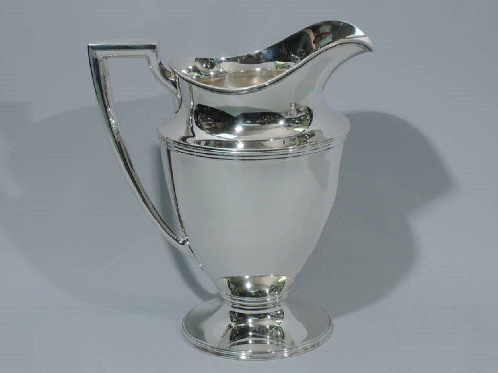 Sterling silver water pitcher. Made by Tiffany & Co. in New York, ca. 1911. Curved and tapering sides, raised foot, scrolled bracket handle, and helmet mouth. Ornamental molding. Heavy. The pattern (no. 18181) was first produced in 1911. Hallmarked.