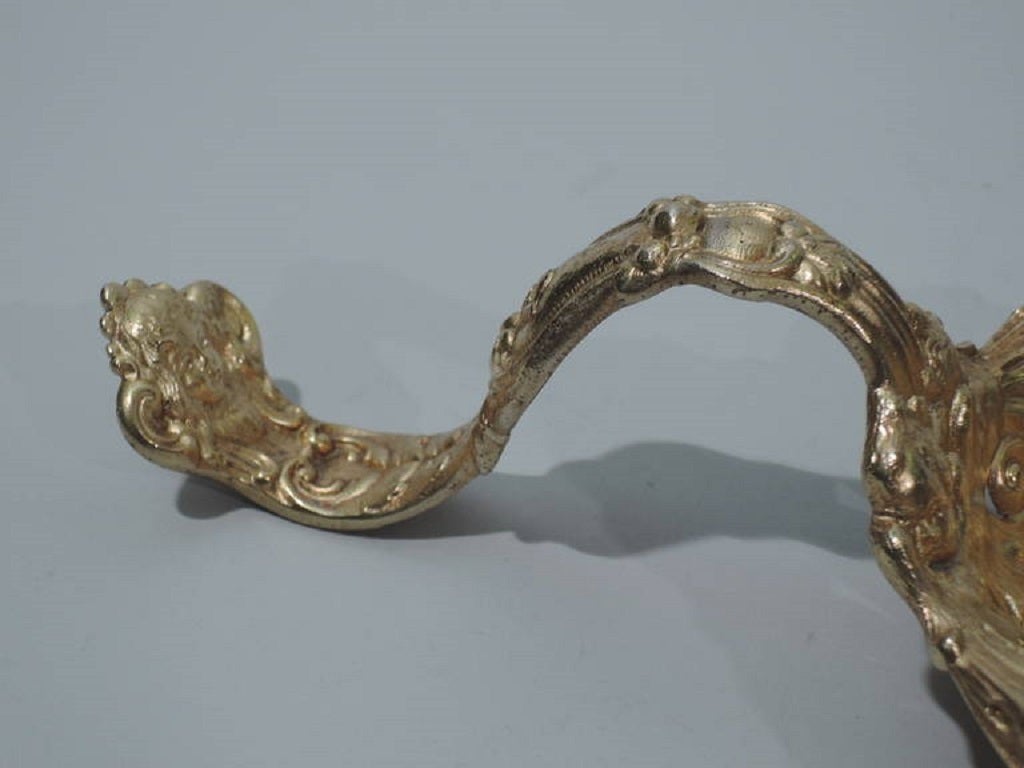 Gilt sterling silver bonbon spoon. Made by Gorham in Providence in 1898. S-scroll handle and round bowl. Bowl has central heraldic cartouche (vacant) and pierced foliage and flowers. Cherubs’ heads and scrolls on handle. Fine details and good heft.