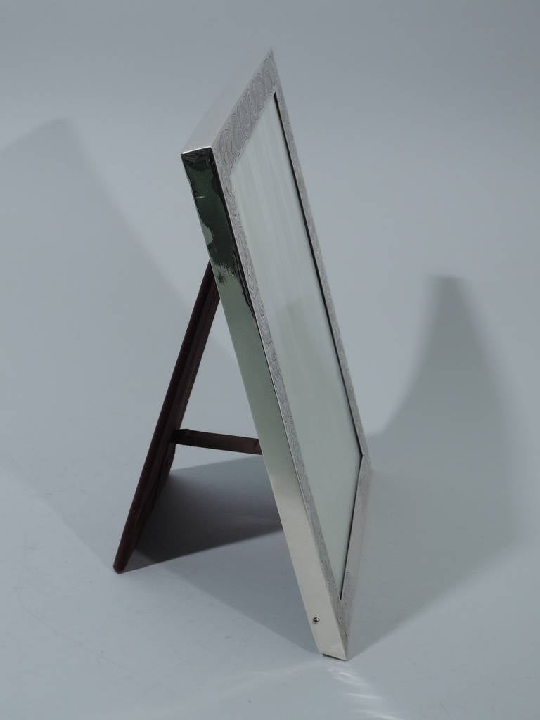 Sterling silver picture frame. Made by Gorham in Providence in 1909. Rectangular window bordered with engraved foliage and scrolls. Part of stretcher vacant for engraving. For vertical photo. With glass, silk lining, and velvet back and hinged