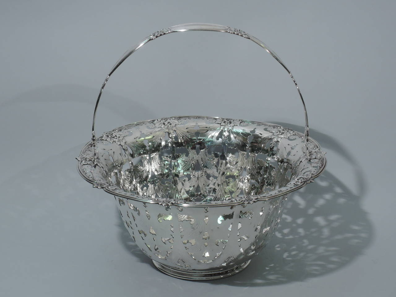 Large and heavy sterling silver basket. Made by Tiffany & Co. in New York, ca. 1910. Tapering sides and flared rim. Rests on molded foot. Solid well. Interior sides are engraved and pierced: inverted arcade with geometric ornament and foliage. Rim