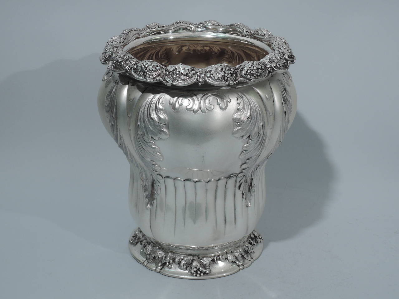 Sterling silver wine cooler. Made by Tiffany & Co. in New York, circa 1886. Baluster form with short neck, turned down rim, and spread foot. Chased and repoussé foliage draped over flutes that encircle lower part. On rim are grape bunches set in