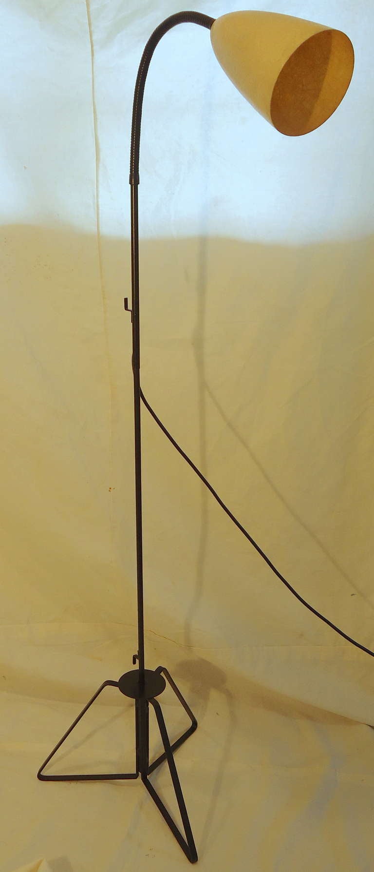 A floor lamp from California manufactured in the 1950s.  
This interesting and unusual early 1950s wrought iron lamp combines flat band iron, iron rod and iron tube with a flexible goose neck which sets in a tripod base. 
The cord can be coiled on