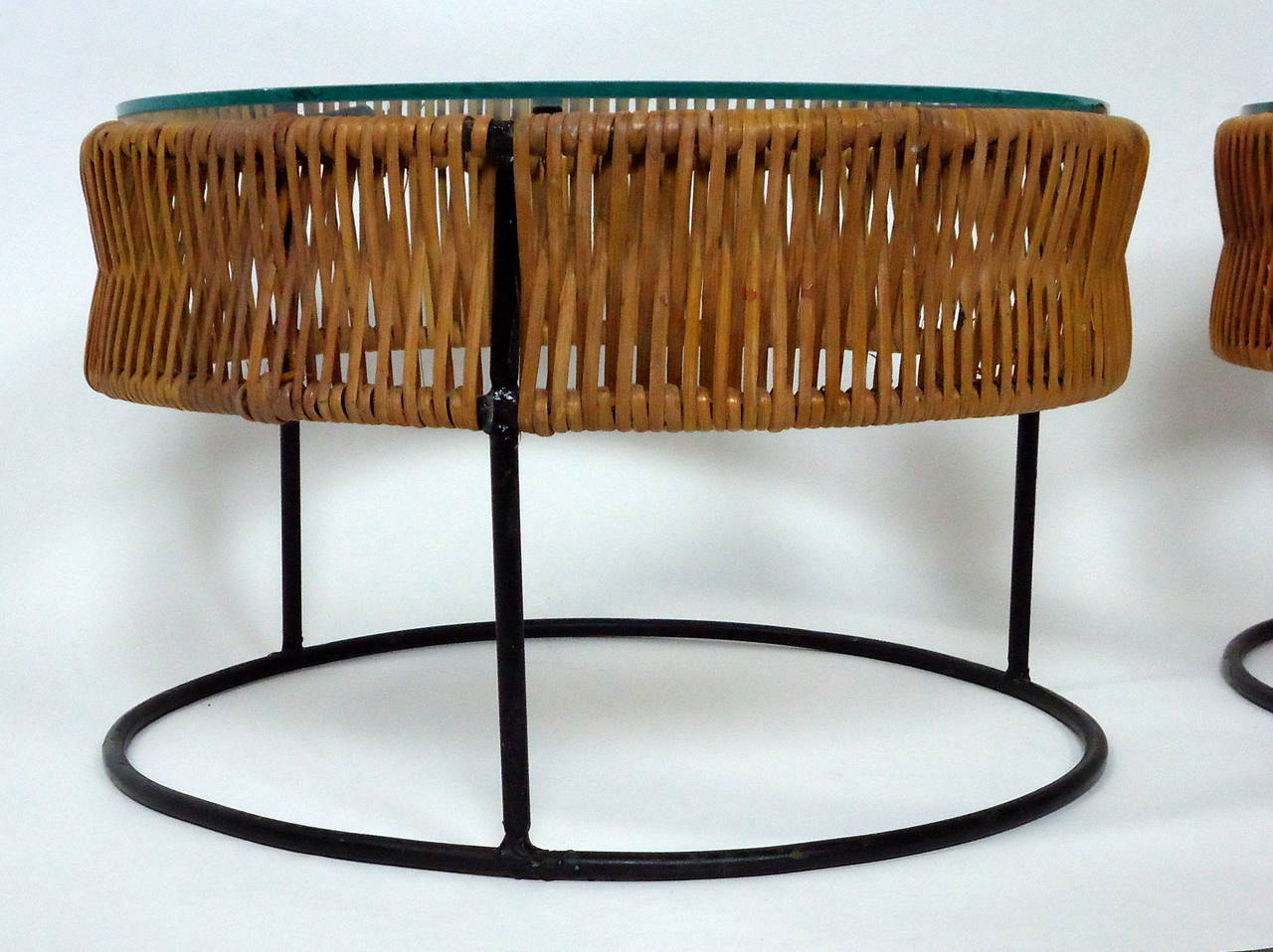 Two glass topped circular black wrought iron wrapped in oval bamboo end tables. 

The pair of Arthur Umanoff tables were commissioned for a Bruce Goff house in 1965. 

The pair have been professionally restored and are in excellent condition.