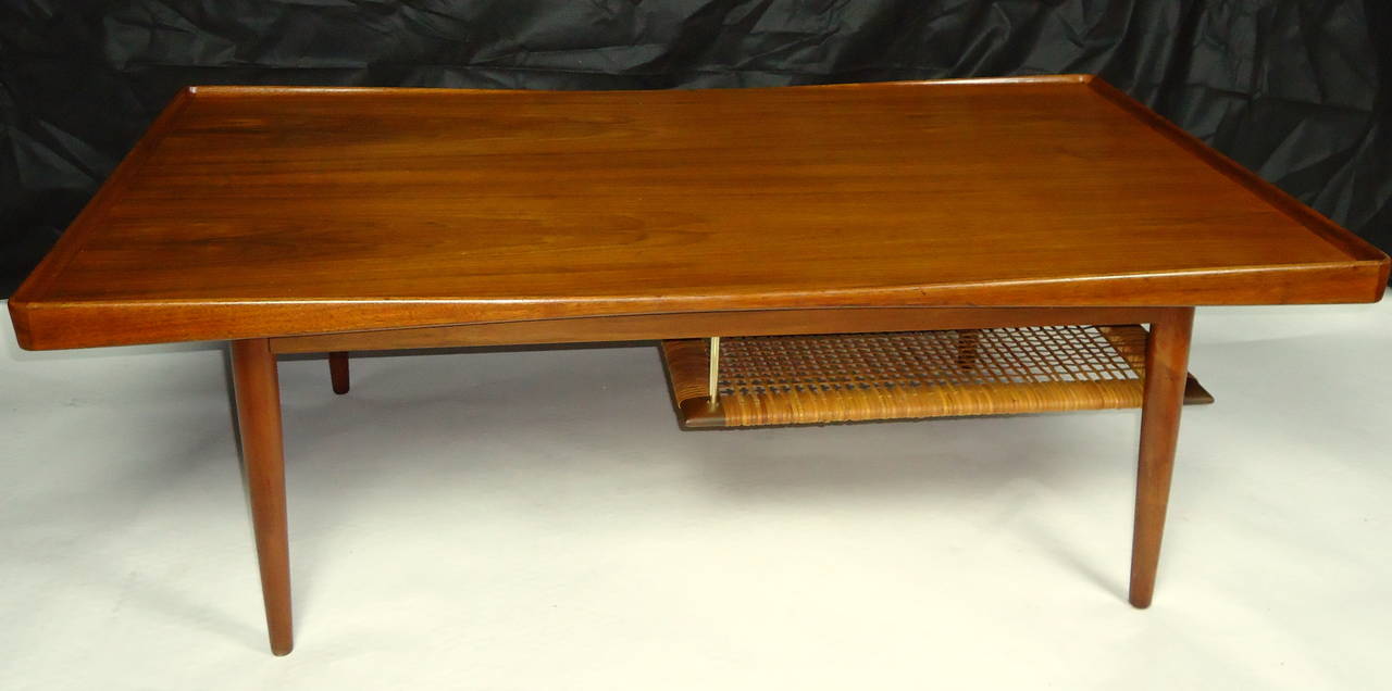 Poul Jensen teak coffee table designed for CFC Silkeborg in the 1950s and imported from Denmark by Selig.
With its sculpted edges, brass tubing and suspended caned shelf it is a classic.
The table and caned shelf are in excellent vintage condition.