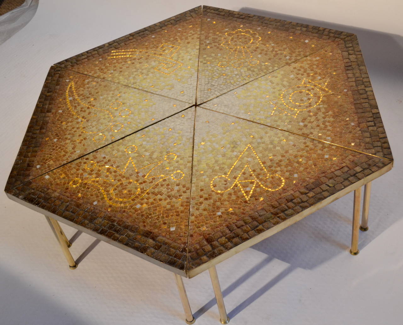 An extraordinary mosaic cocktail table edged in brass with brass legs by Genaro Alvarez created at his Mexico City studio in the mid-1950s.

Each of the 6 triangular tables has an Aztec symbol and randomly placed pieces of gold mirror tile set