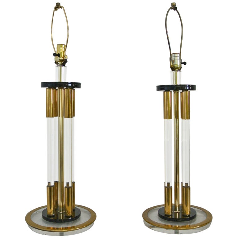 A sophisticated pair of vintage Lucite and brass table lamps. Each lamp has a central brass tube surrounded by four clear Lucite tubes. Each tube capped on each end in brass-mounted between two black Lucite disks on a circular base of clear Lucite