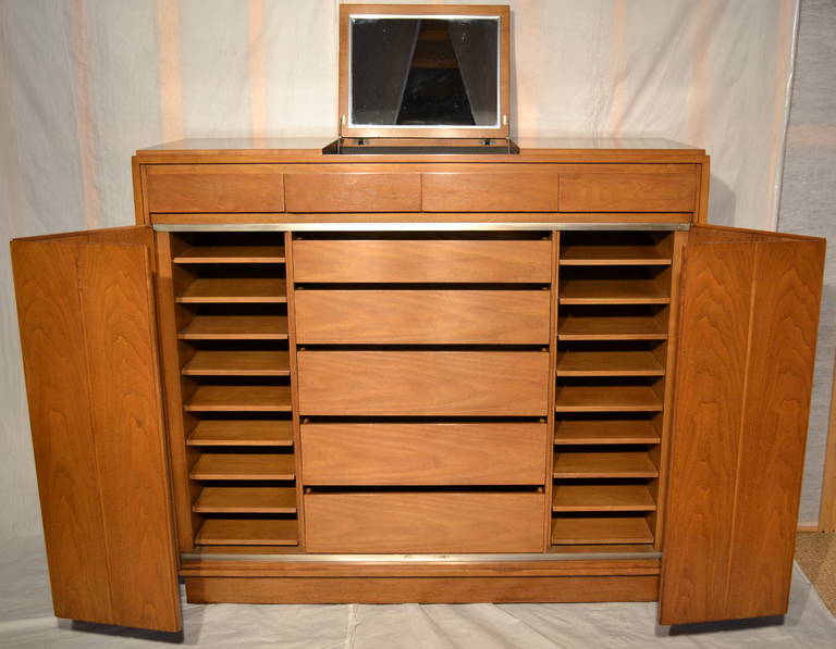 A rare design by Paul McCobb for Widdicomb.

This well composed walnut tall dresser designed in the early 1960s.

The cabinet has a pair of accordion doors and a lift up mirror there are 18 individual sliding shirt trays with a central stack of