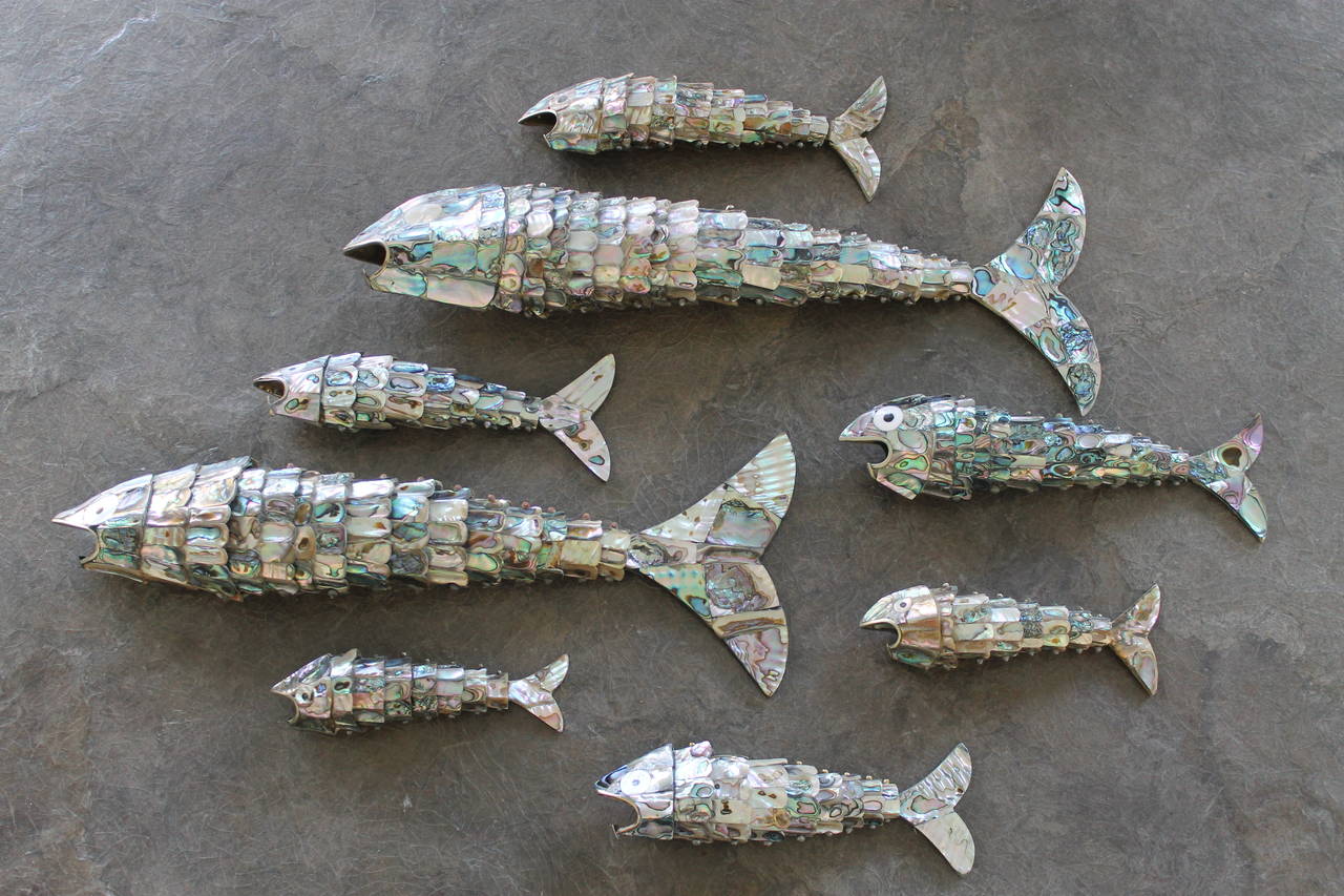 A collection of vintage Mexican articulated abalone fish. A set of eight circa 1960's to 70's articulated fish bottle openers all covered in abalone mosaic. Metals used are brass and Alpaca silver. There are a few missing abalone pieces here and