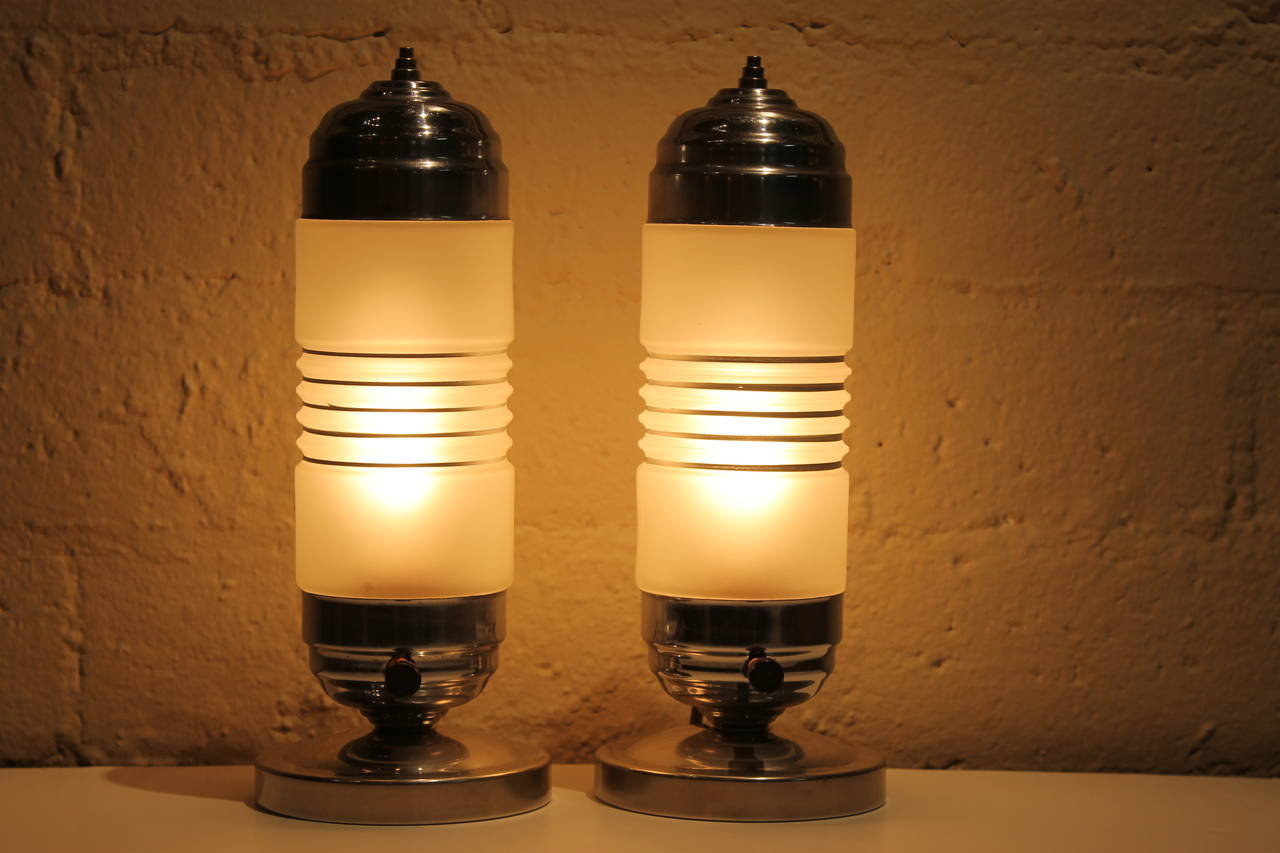 A matched pair of circa 1930s chrome lamps with frosted glass shades. Hand painted silver stripes encircle each shade. Bases are chrome plated steel as are the tops which have chromed brass finials. Height is 11.25