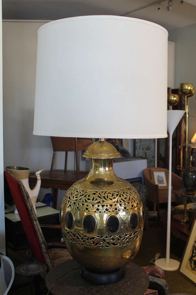 A massive bulbous form hammered brass table lamp set with twelve natural horn medallions, all bezel-set like cameos. Lots of hand tooling, with three bands of scrolling openwork. Black painted wood base. The brass element alone measures 24” tall and