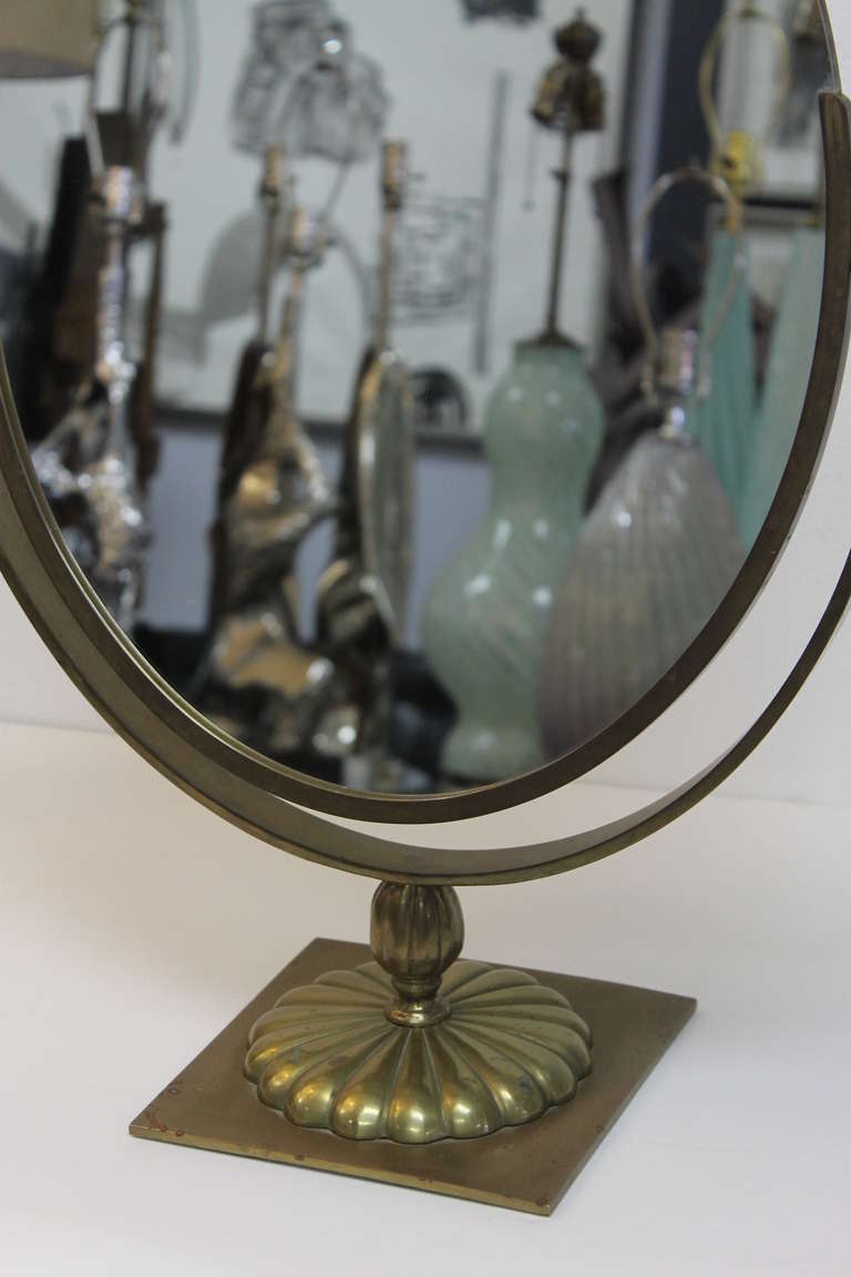 A handsome brass counter mirror from a Saks Fifth Avenue store circa 1950’s. Heavy and well constructed, this mirror features a double-sided swiveling oval glass. There is one small spot on the edge of the mirror where a speck of the silvering has