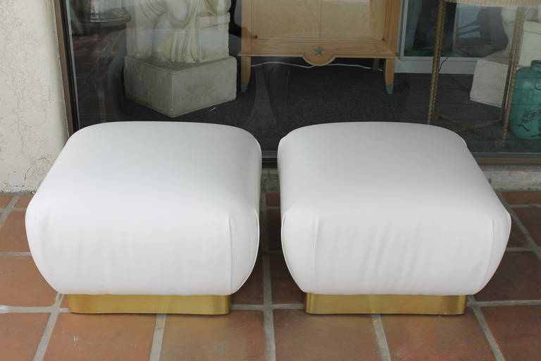 Pair of newly upholstered white leather ottomans on wood base with brass lining.  There's a label which is available.  Manufactured by Marge Carson, Inc.  9056 Garvey Boulevard Rosemead, Ca 91770.  The ottomans measure 26" square and 18"