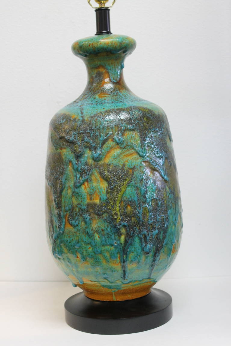 A large ceramic table lamp with very thick and drippy lave glaze in shades of turquoise, blue, and orangey gold. Dimensions of the ceramic element alone are 23” high and 12” at its widest.  Overall height of the lamp to the bottom of the socket is