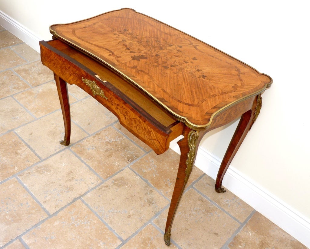 A Nineteenth Century French side table with a shaped top decorated throughout in scrolling floral marquetry. The table is embellished with finely chased gilt bronze mounts running the length of the cabriole legs.