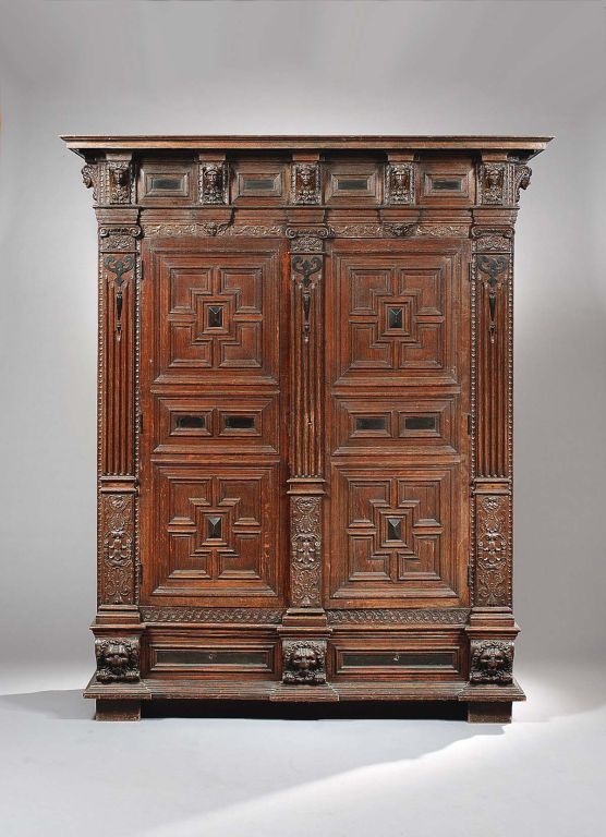 A monumental Flemish Oak and Ebonised cupboard from the Saxe-Coburg-Gotha collection. The frieze top is decorated with carved heads divided by ebonised panels. The doors feature ebonised panels set within geometric borders, each door is flanked by a