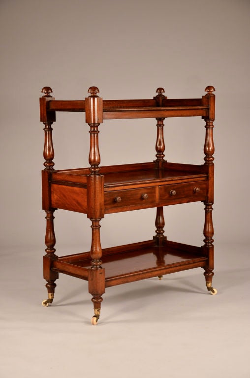 Mahogany trolley with three lipped shelves and two drawers, all on casters.<br />
<br />
The posts have mushroom shaped finials, bold baluster and ring turnings between squared supporting sections.<br />
 <br />
This trolley has excellent rich