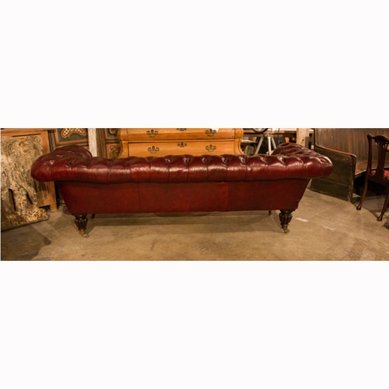 A beautiful 19th century Victorian red leather chesterfield sofa accented with deep buttons and nailhead trim with walnut frame and brass caster.
