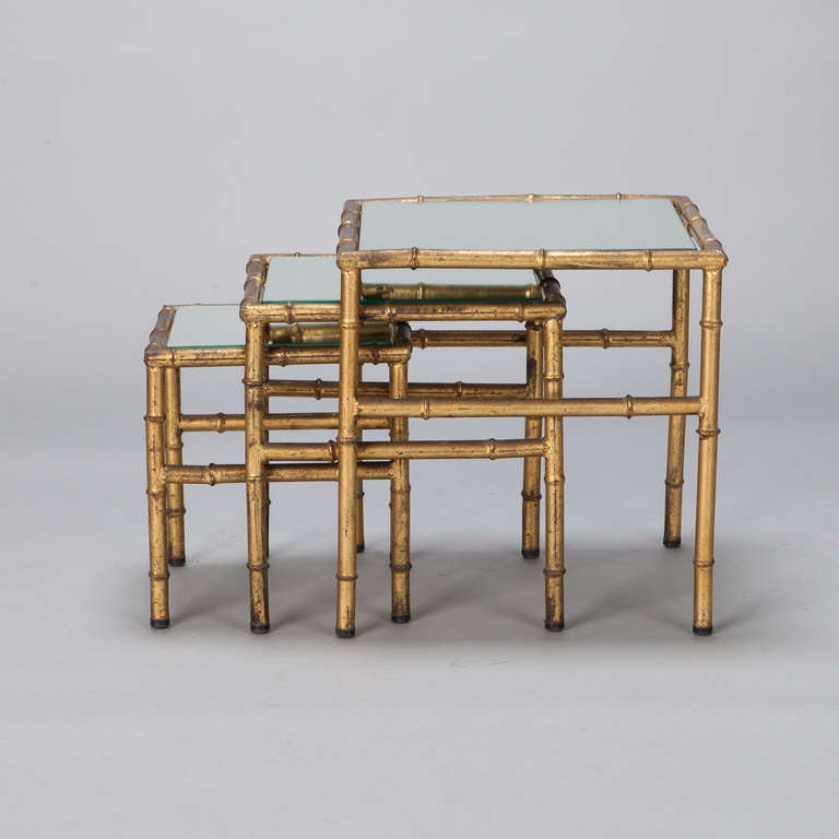 Set of Italian gilt metal nesting tables with mirrored tabletops and faux bamboo style base. Sold and priced as a set. Measurements shown are for the largest table, circa 1940s.