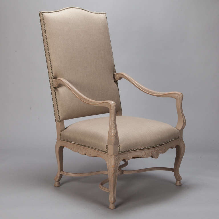 Tall French armchair with high upholstered back, carved details on the arms, legs and apron, and new neutral-colored upholstery with decorative nailheads, circa 1900. Arms are 31” high, seat is 18.5” high and 24” deep.