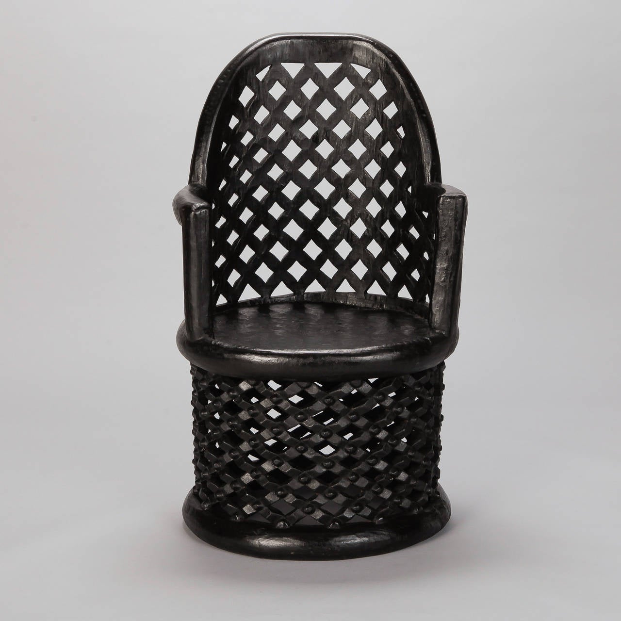 Carved Bamileke spider armchair from Cameroon, circa 1980s. hand-carved dark wood armchair with rounded, open-work back, round seat and open work pedestal base. Two available - sold separately.

Chair #1:
23” W x 37.5” H x 23” D.
Arm height: