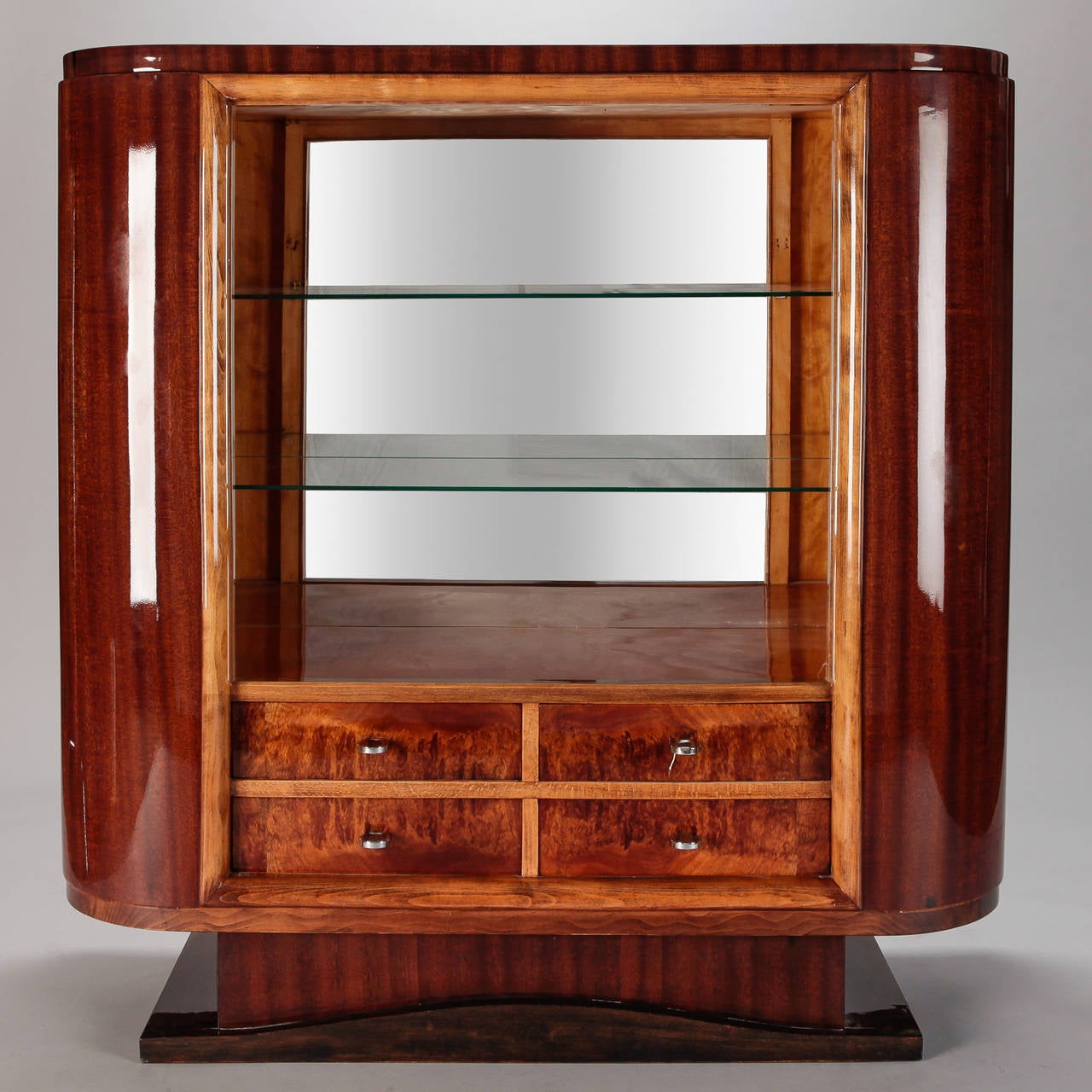 Circa 1930s French cabinet has a dark wood base, cabinet and drawers in contrasting polished blonde wood and darker wood with open glass shelves in the center and mirror back. Silver tone hardware. Elegant Deco-era curves. Makes a great piece for