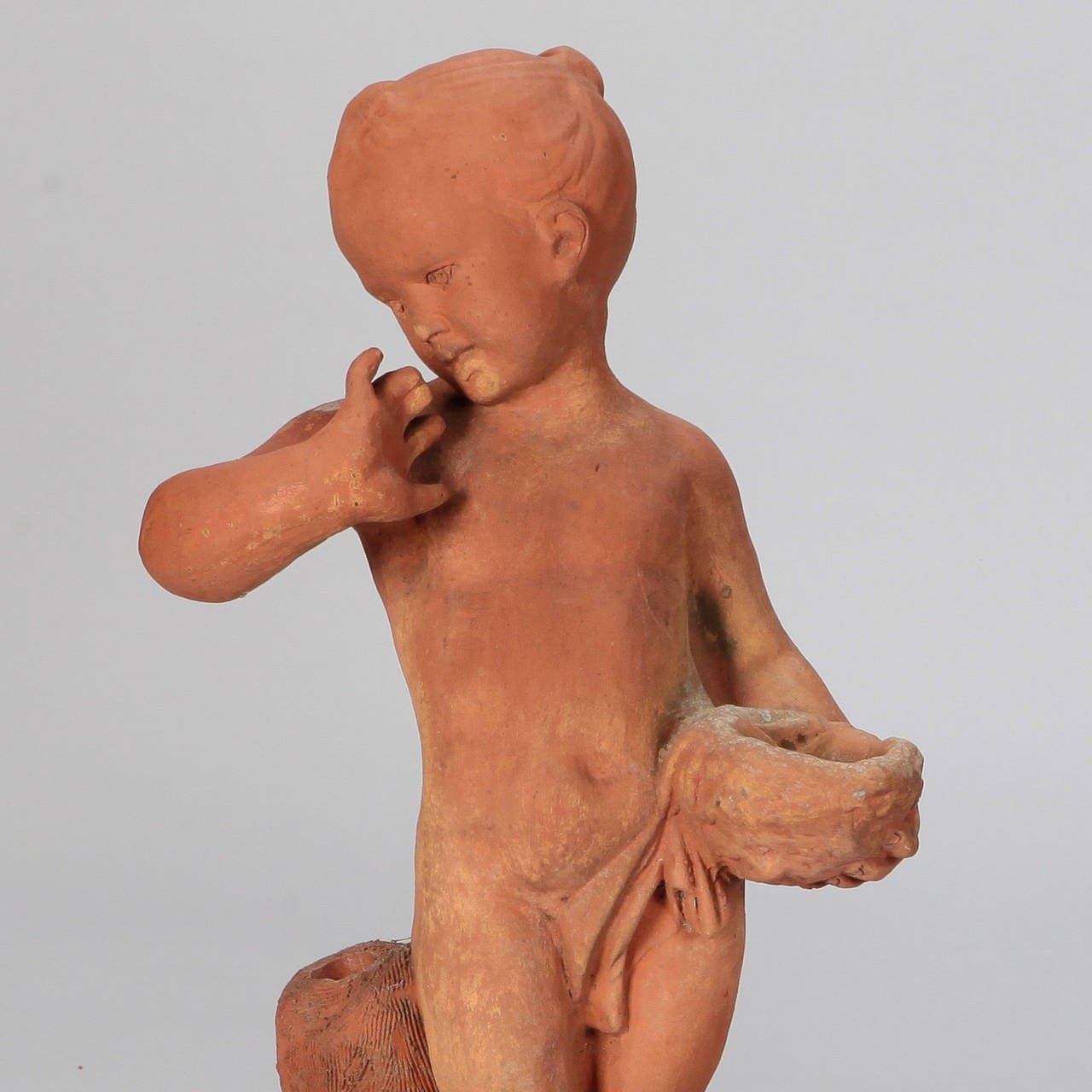 Circa 1940s pair of French terra cotta garden statues. One child (smaller) holds a bowl and the other wears a plumed hat. Some surface wear and repairs. Repaired base on statue of child with bowl; statue of child with hat is missing part of hat brim