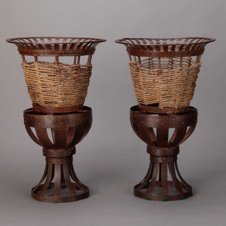 Circa 1930s tall iron jardinieres with open work pedestal and urn form body accented with woven jute. Sold and priced as a pair.
