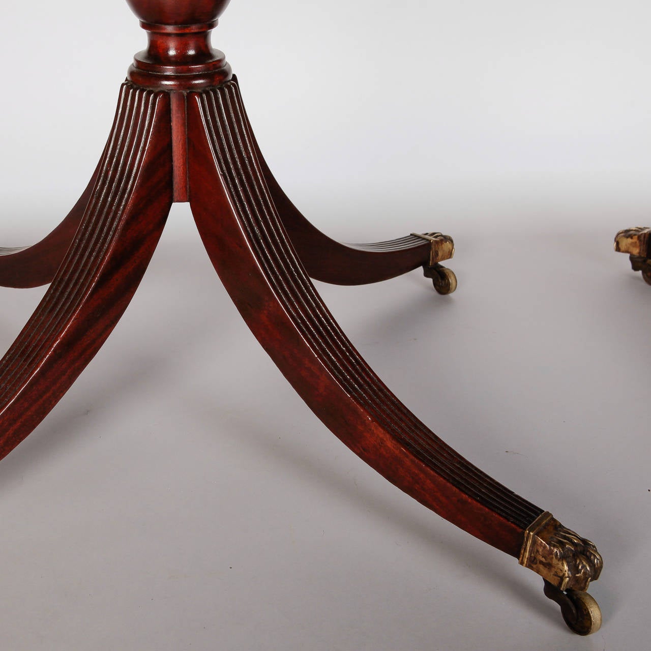 Circa 1900 oval English mahogany table with three pedestal bases. Removable center section leaf is 36” wide. Table legs are reeded with solid brass claw feet and casters.