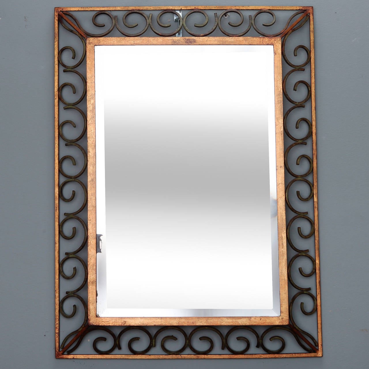 Rectangular beveled edge mirror with open work scroll frame in gilded and green painted iron, circa 1930s. Actual mirror size: 24.75” H x 16.5” W.