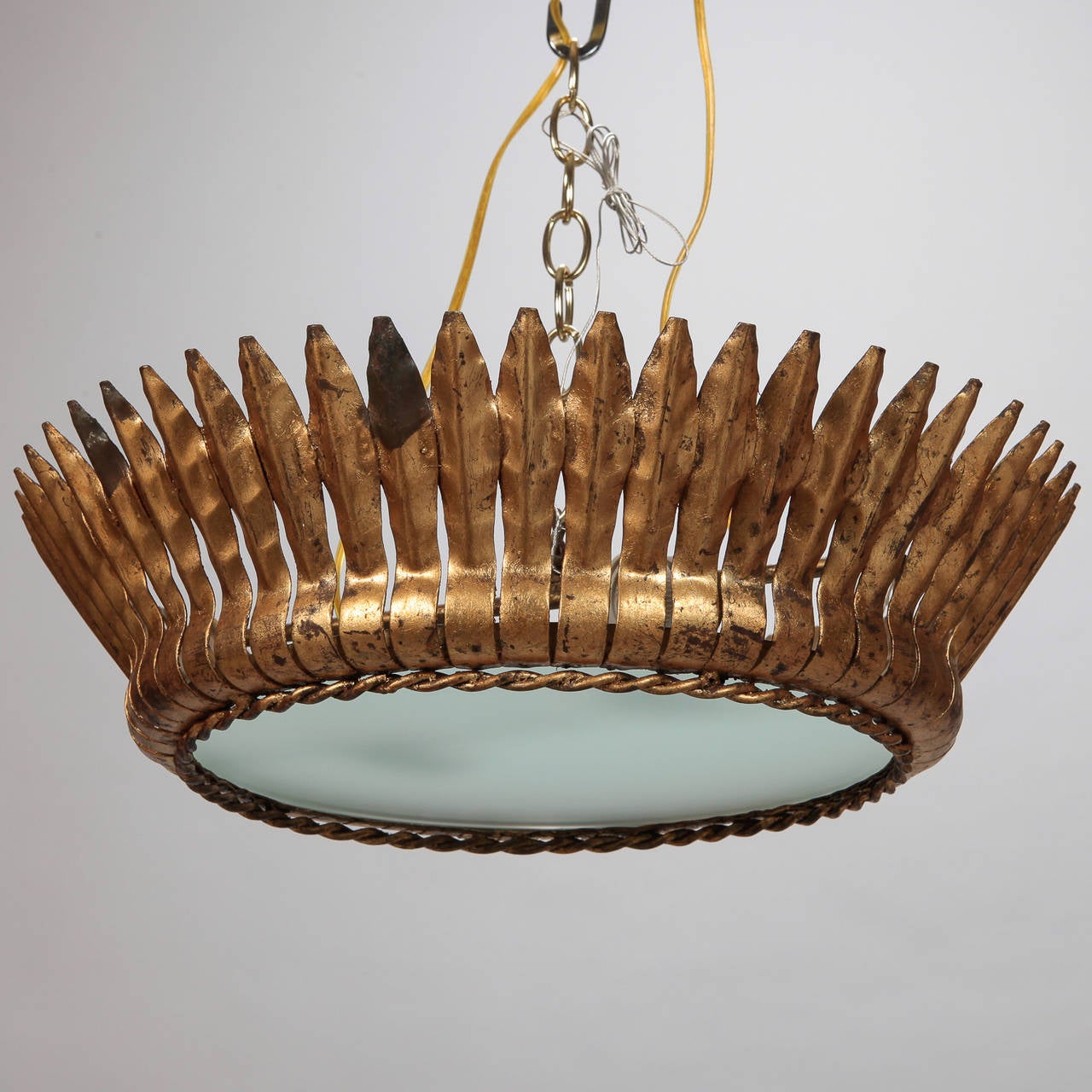 Circa 1950s sunburst / starburst shaped gilt metal hanging fixture has round center of white satin glass framed with uniform rays suspended from central chain. Inside are two full size light sockets that have been updated for US electrical