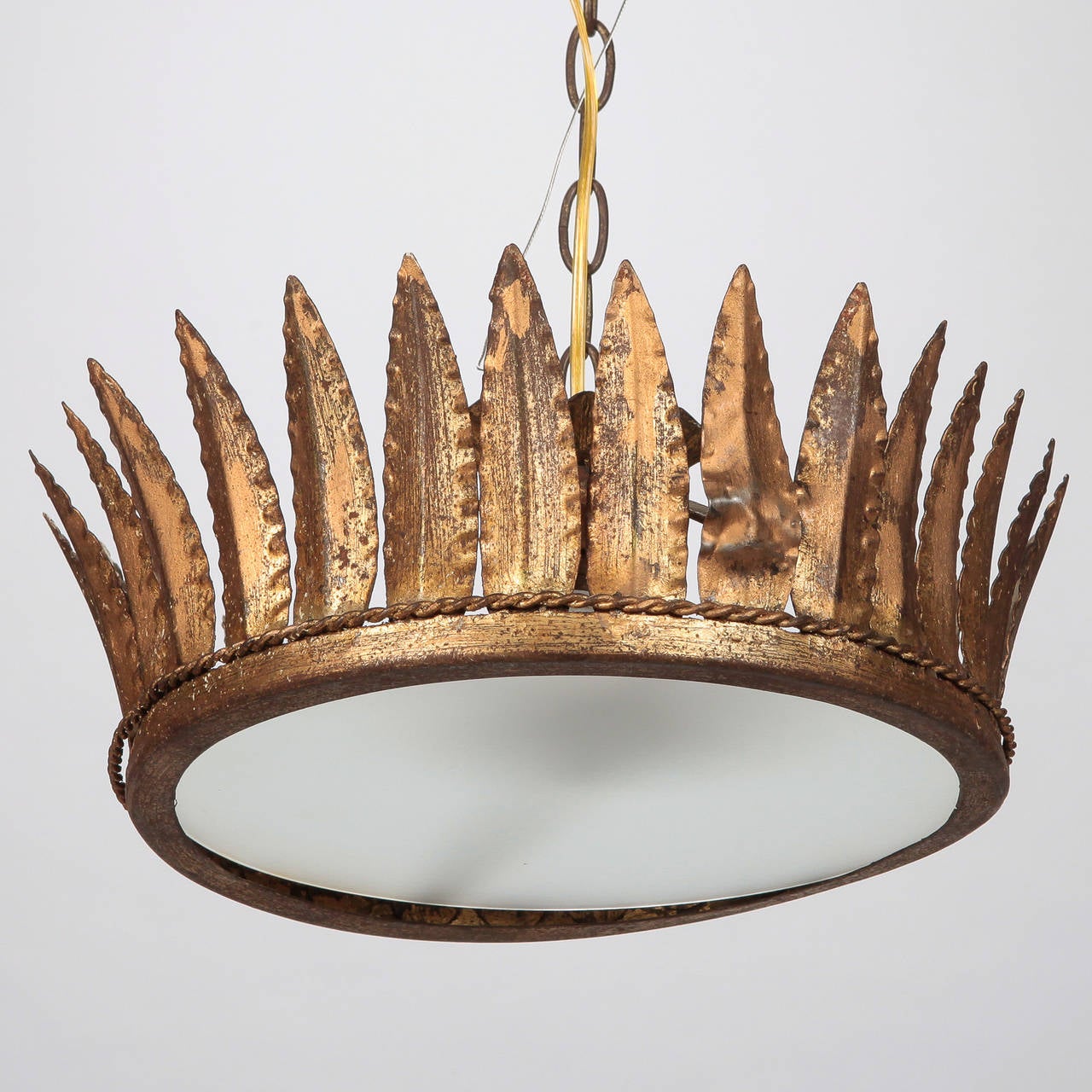 Circa 1950s Spanish gilded metal hanging light fixture has a single full size light socket behind white satin glass center framed with small twisted border and gilded leaf form rays. Suspended from center chain with new electrical wiring for US