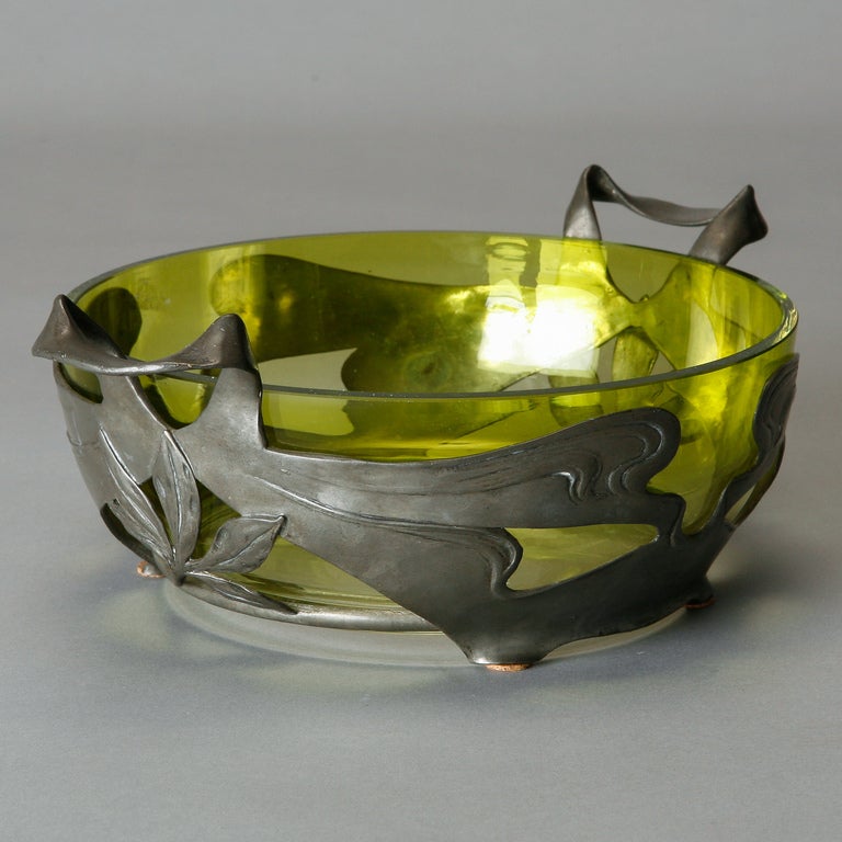 
French art glass bowl in a pale green has a footed pewter surround with an abstract Art Nouveau design and curved handles. 