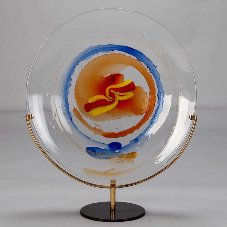 Circa 1980s large Murano art glass plate signed by renowned artist Mario Badioli. Colorful, abstract design in vivid shades of orange, red and blue. Brass and metal display stand is included.