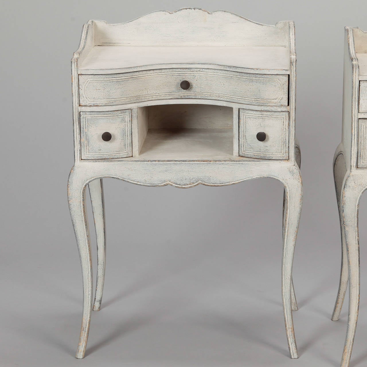 Circa 1920s pair night tables with antique white painted finish, cabriole legs, curved fronts and three small drawers. Sold and priced as a pair.

Tall Point - Back Scallop:  27.5”
Shelf Ht:  24”