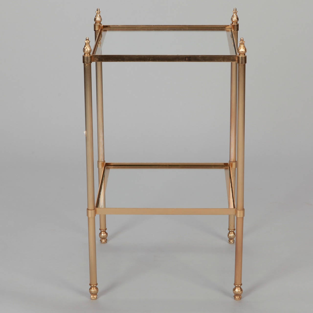 Neoclassical brass and glass two-tier side table with sculpted finials, circa 1960s.