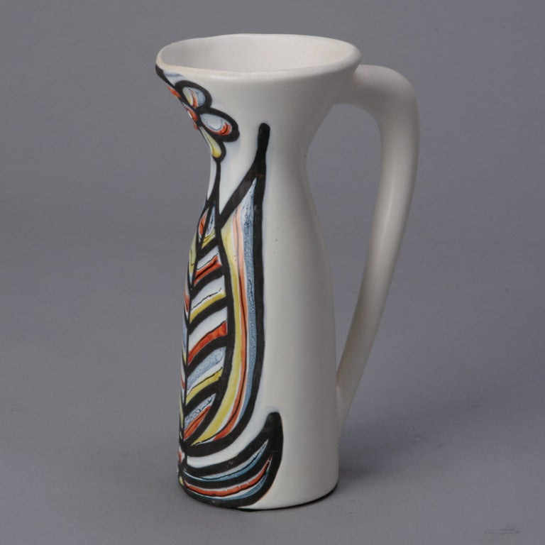 Circa 1940s Vallauris modernist pitcher by Roger Capron has a creamy white matte glaze with a colorful flower and leaf.  Signed by the artist. We have several other Capron pieces in other shapes in similar glazes.  Please inquire.