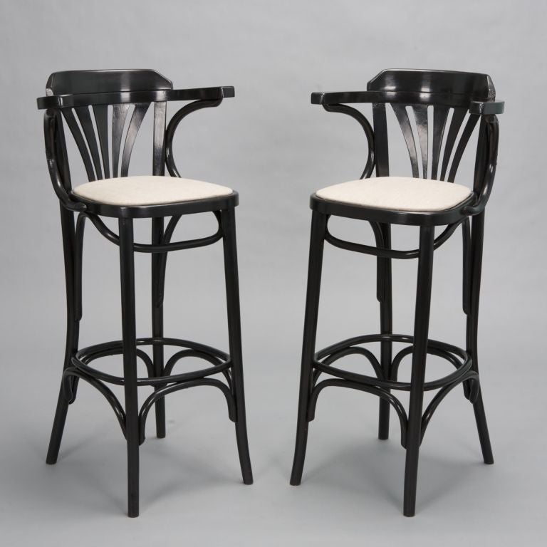 These tall French bentwood bar stools have arms, graduated slat backs, bentwood foot rests and side arches, and upholstered seats. Seat height is 30