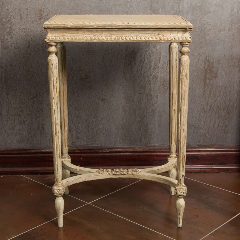 Circa 1920s French rectangular side table with antique white painted finish, tapered and reeded legs, decorative feet and a curvy,  X-base stretcher with ornamental floral carving. 